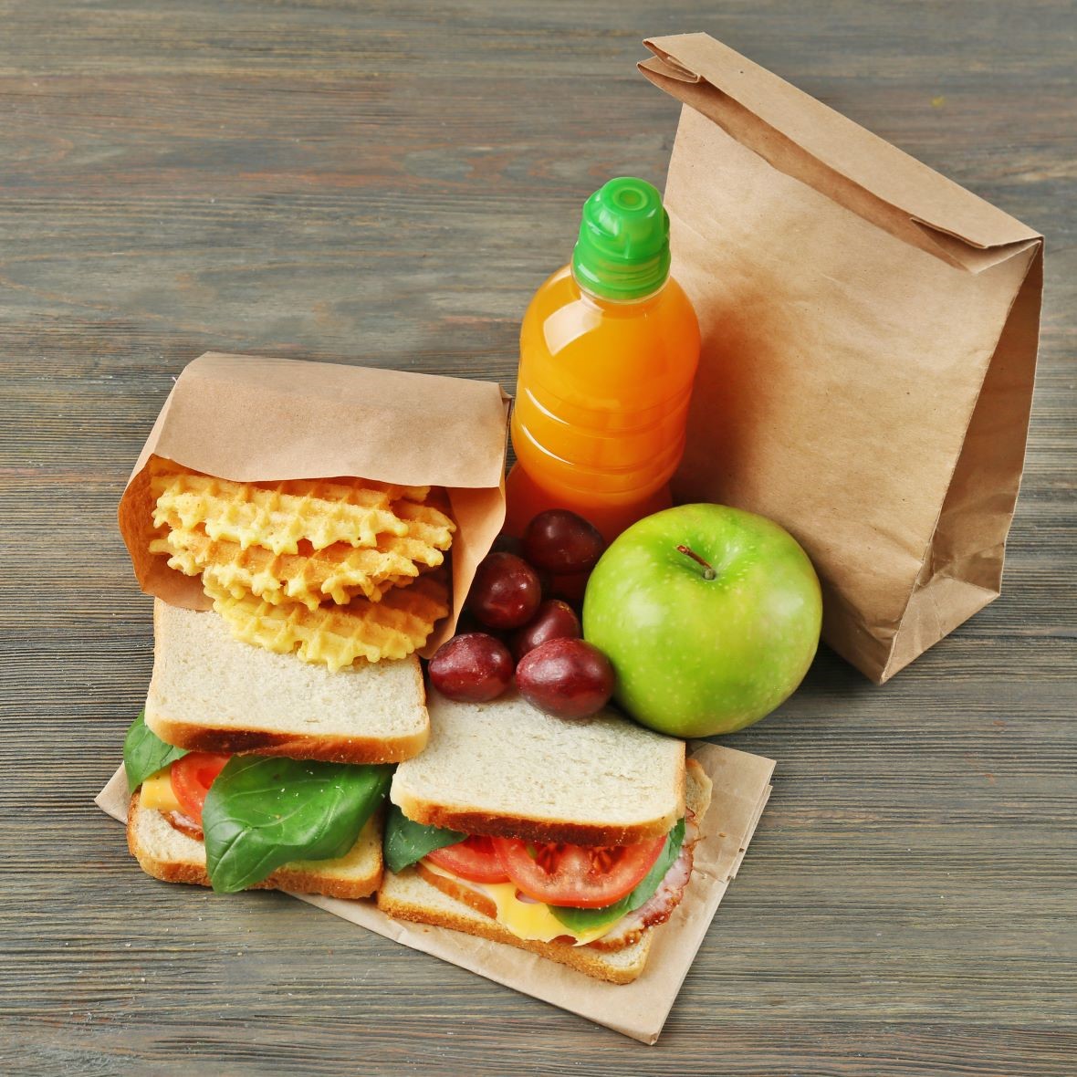 Brown paper bag with sandwiches, pastries, fruit, and a drink.