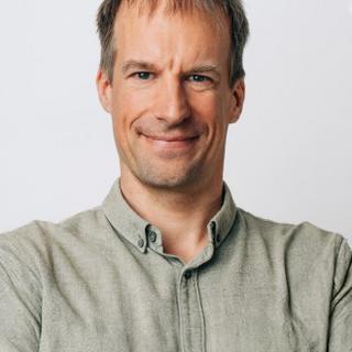 Smiling man with short hair and crossed arms, wearing a light green shirt against a white background.