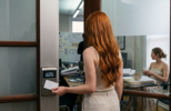 Persona utilizando una tarjeta de acceso para entrar en una sala de reuniones de oficina, mientras varias personas trabajan y colaboran en el interior. La imagen representa el acceso a nuevas tecnologías y la adopción de la inteligencia artificial en el entorno empresarial.
